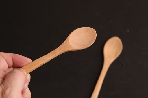 An overhead shot of a person holding a small wooden spoon with a dark blurry background