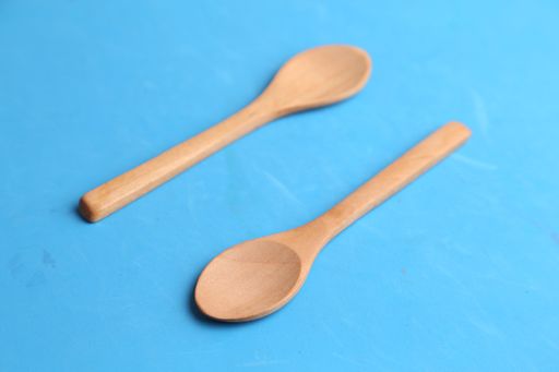 A closeup of two wooden ladles pointing on the opposite direction on a blue surface
