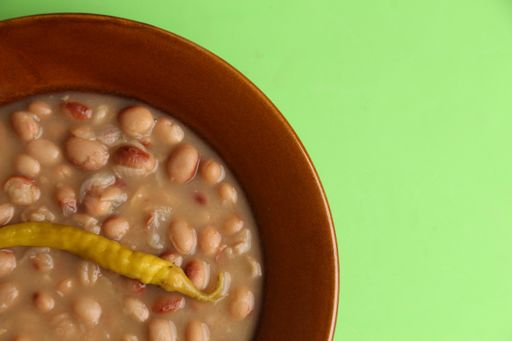 A high angle shot of a plate of bean soup with pepper isolated on a green surface