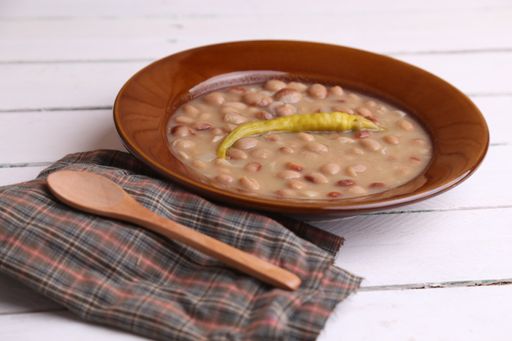 A high angle shot of a bowl of ban soup with pepper on a cloth on a white wooden surface
