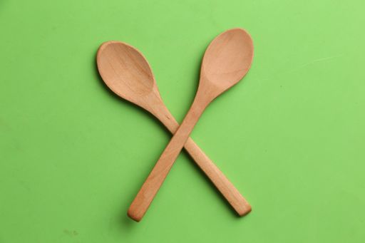 An overhead shot of two crossed wooden spoons on a green surface