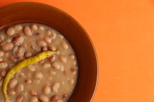 An overhead closeup shot of a bowl of delicious bean soup with a spicy pepper on an orange background