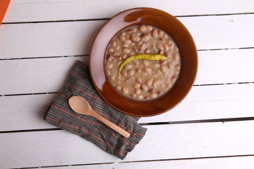 A top view of a bowl of typical Spanish dish, red beans with chili pepper on a white wooden surface