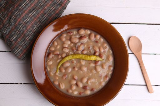 A closeup of the delicious bean soup with a spicy pepper in a brown bowl
