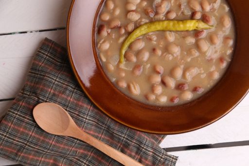 A top view closeup of a bowl of bean soup topped a yellow cayenne with a wooden spoon and patterned cloth on the side