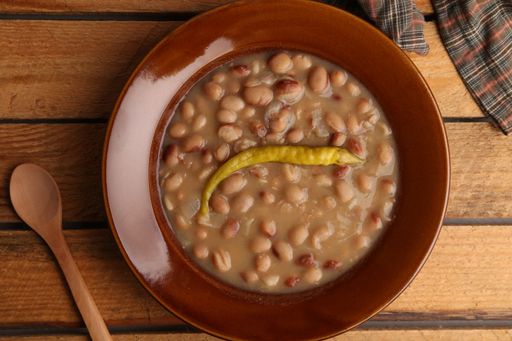 A high angle shot of a plate of bean soup with pepper isolated on a wooden surface