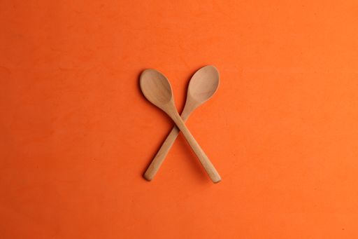 A flat lay shot of two wooden spoons on an orange surface