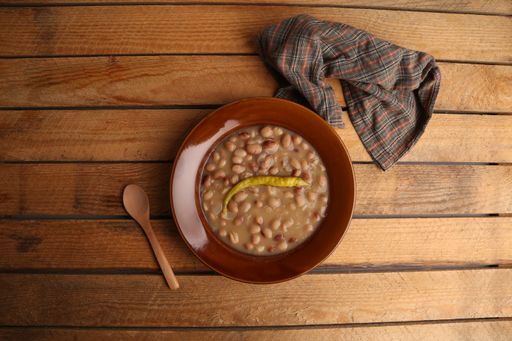 A high angle shot of bean soup with pepper in  bowl  and spoon on  the side