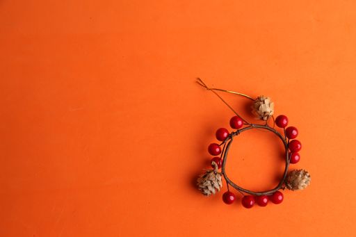 A high angle shot of a wooden ring decorated with fake berries and pine cones on an orange surface