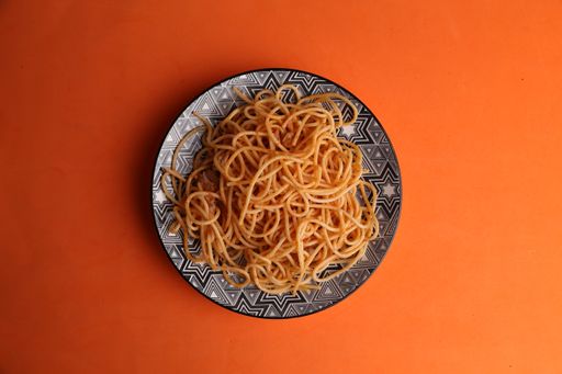 An overhead shot of spaghetti noodles in a patterned plate on an orange surface