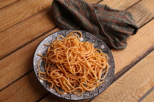 A high angle shot of a plate of delicious spaghetti with tomato sauce on a wooden surface