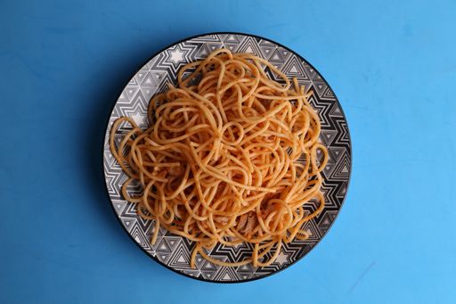 A high angle shot of a plate of delicious spaghetti isolated on a blue surface