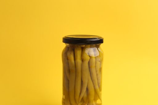 A selective focus shot of a jar filled with peppers isolated on a yellow background