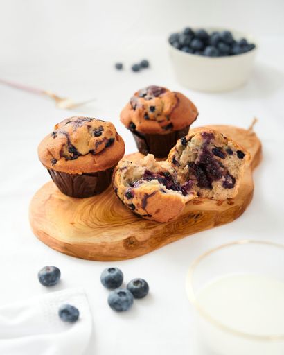 A vertical shot of homemade delicious blueberry muffins with one broken open