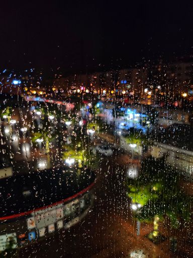 A vertical shot of blurred illuminated buildings through a wet glass