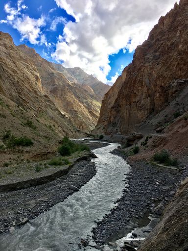 A vertical shot of a muddy river flowing at the foot of bare mountains in Ladakh, India