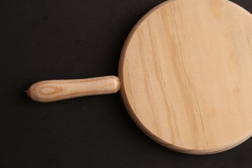 A flat lay shot of a chopping board with a handle on a black surface