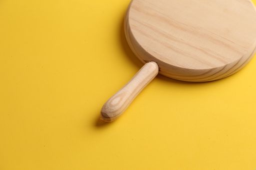 A high angle shot of a round wooden board on a yellow background