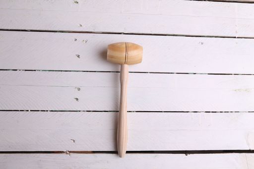 An overhead shot of a small wooden mallet on a  white wooden background
