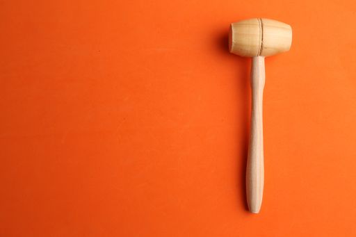 An overhead shot of a wooden mallet on an orange background