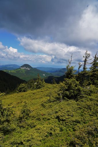 A beautiful landscape of mountain range and green hilly valley with thick clouds in the blue sky.