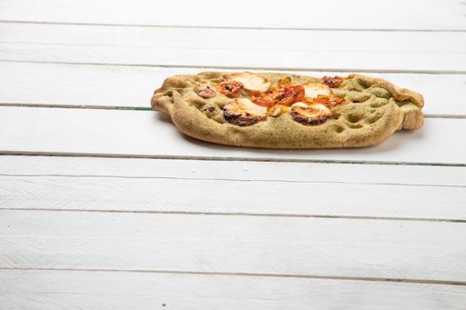 A bread with pesto, tomato, and goat cheese isolated on a white wooden surface