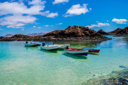 A vibrant tropical landscape featuring colorful boats floating on crystal clear waters, with a lush island in the background under a bright blue sky.