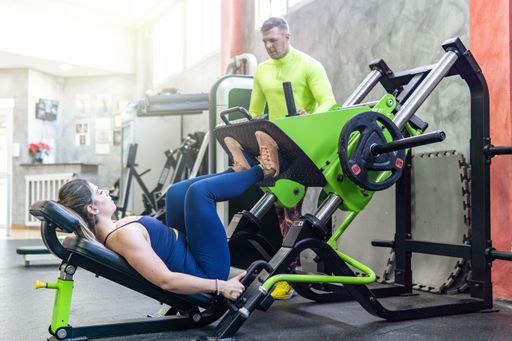 Personal trainer coaching a young caucasian woman, legs exercises with machine in the gym, workout concept