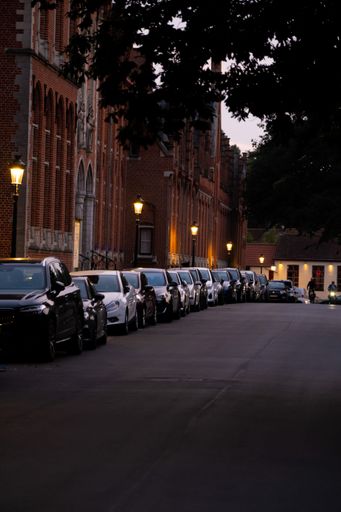 A vertical shot of the row of parked cars on the roadside near a red brick building.