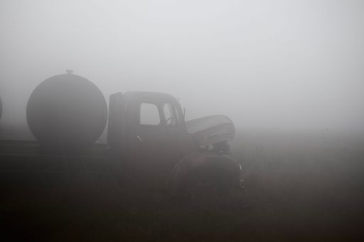 A rusty abandoned old broken down truck on a misty field