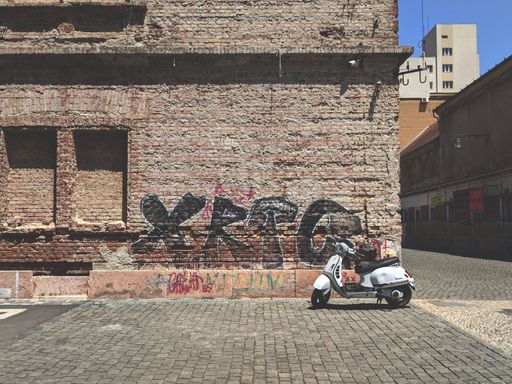 A white scooter at a brick wall with graffiti in town