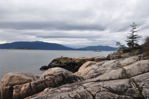 The rocky shore against the lake, hills and cloudy sky. West Vancouver, British Columbia, Canada.