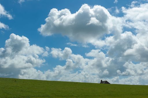 A low angle shot of the rood of small house on lush green hilltop in Germany against blue cloudy sky