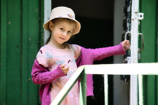 Cute girl in a hat looking at a camera. while holding a door open to her room in a summer camp.