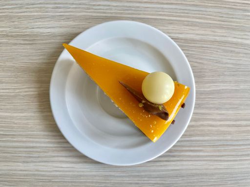 A piece of delicious passion fruit cake decorated with white chocolate ball on a white plate lying on a wooden table.