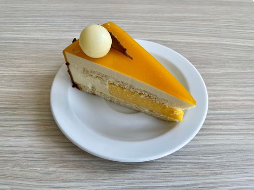 Slice of delicious passion fruit cake with withe and milk chocolate decoration on a white plate on wooden table