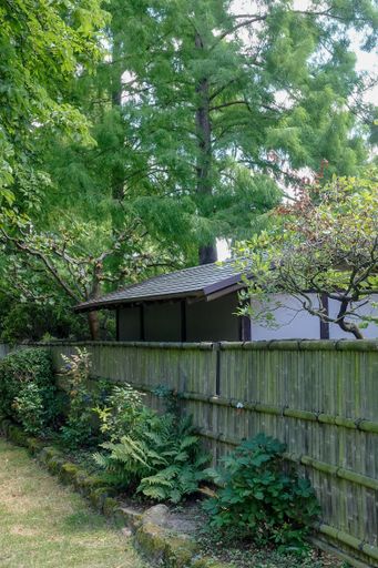 A vertical shot of a shed behind the fence made out of bamboo sticks in a garden during daylight