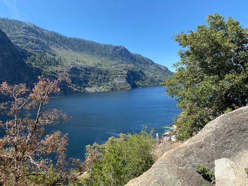 An aerial view of blue lake surrounded by green mountains on blue sky background