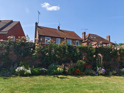 The colorful flowers on and by stone fence with red brick houses in the background