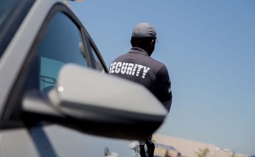The security person standing near a car at parking lot, shot from back