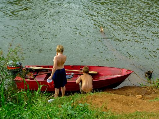 A high angle shot of an old red-painted boat in a river with two boys standing close