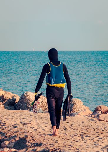 A rear view of a young surfer walking on a sandy beach at daytime in Pristina, Kosovo