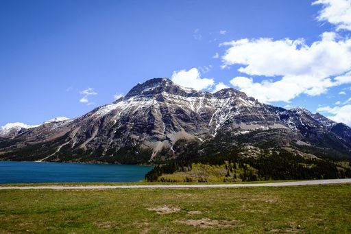 An aerial view of greenery field near lake in background of snow covered mountains
