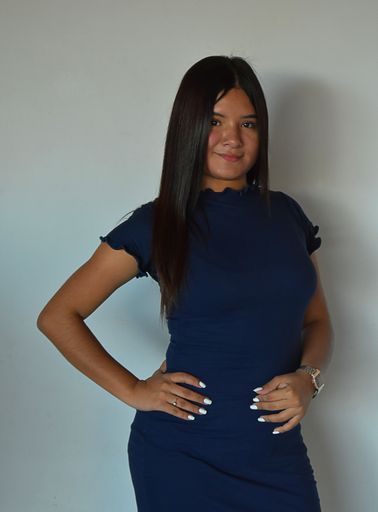 A vertical shot of a beautiful young Latino female with a blue dress posing in front of a white wall