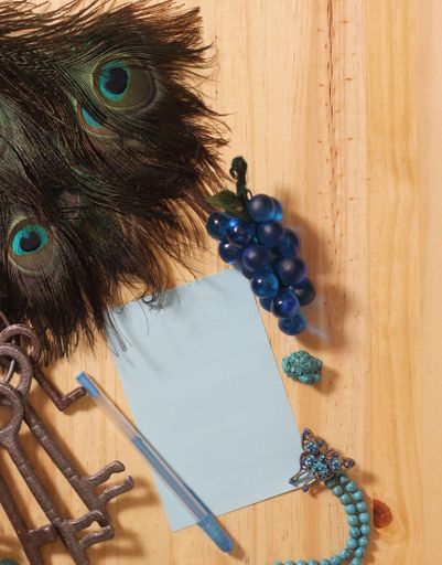 Notepaper and Pen on Wooden Table Surrounded By Peacock Feathers and Jewelry