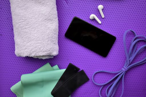 A top view of a mobile phone with gym equipment and wireless earphones on a gym mattress