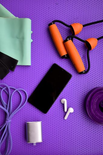 A flat lay of fitness training items, a phone, and headphones on a purple fitness matte