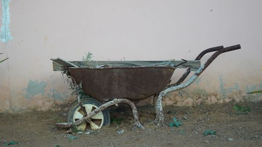 The close-up view of an old brown wheelbarrow in the soil before the wall