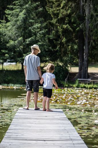 A vertical shot of a boy and his little sister standing on the edge of a pier by the lily pond