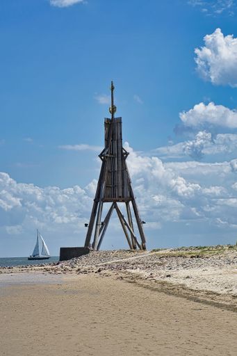 A vertical shot of the Kugelbake historic day beacon against cloudy blue sky